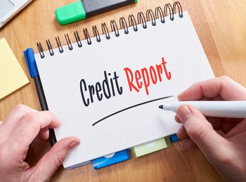 Someone holding a pen and writing on a notebook that says credit report