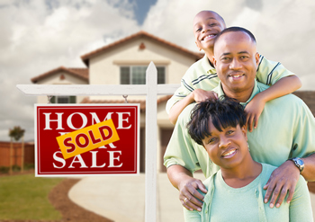 Happy home buyers standing next to a for sale sign with a sold sticker
